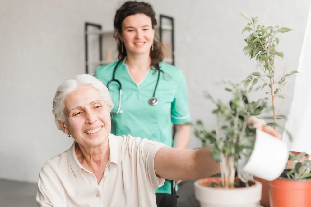 Pflegekraft mit einer Seniorin, die eine Pflanze gießt